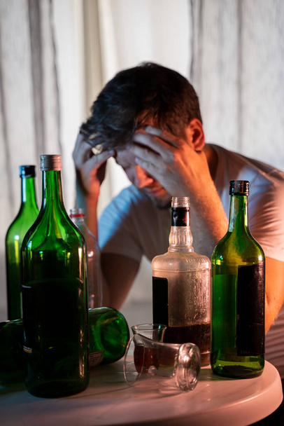 σιλουέτα μιας σιλουέτας ανώνυμου αλκοολικού που πίνει πίσω από μπουκάλια αλκοόλ, αλκοολισμό - Φωτογραφία, εικόνα