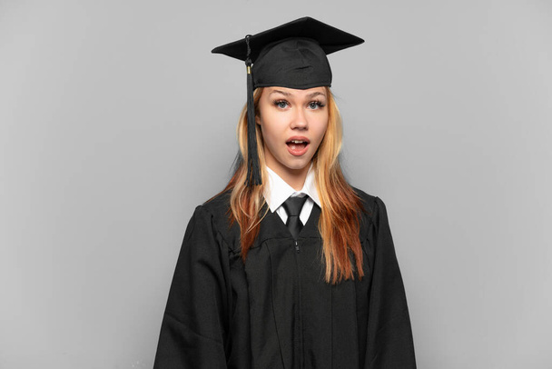 Молодая выпускница университета на изолированном фоне с неожиданным выражением лица - Фото, изображение