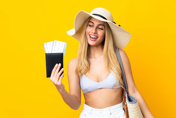 Young Uruguayan blonde woman in swimsuit holding a passport over isolated yellow background with sad expression - Foto, imagen