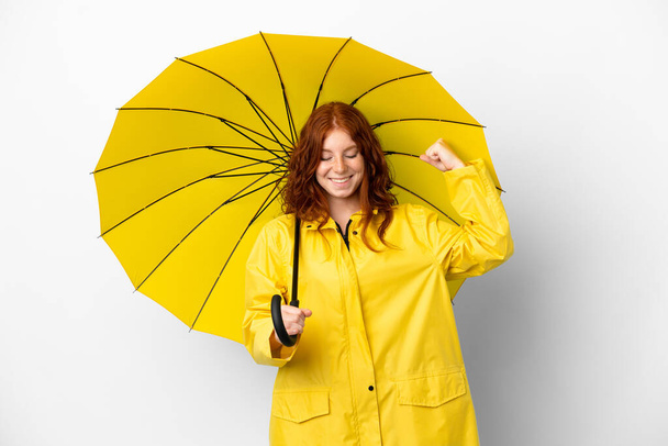 Adolescente ruiva menina capa impermeável e guarda-chuva isolado no fundo branco fazendo gesto forte - Foto, Imagem