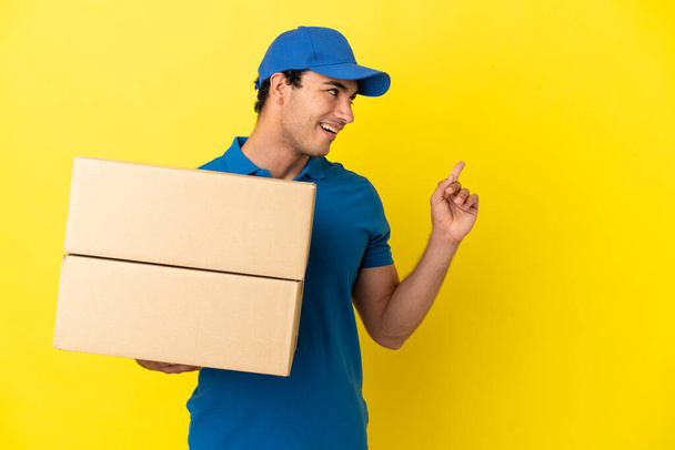Delivery man over isolated yellow wall intending to realizes the solution while lifting a finger up - Photo, Image