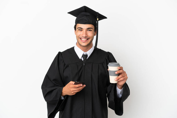 若い大学卒業生隔離された白い背景にコーヒーを持って離陸し、携帯電話 - 写真・画像