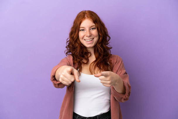 Adolescente pelirroja chica sobre aislado púrpura fondo sorprendido y apuntando frente - Foto, Imagen