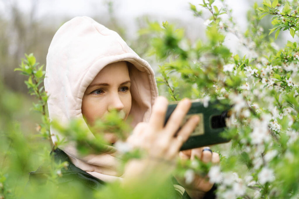 Phone lenses for macro photography. A woman holds a mobile phone with a macro attachment in her hands and takes pictures of plants. - Zdjęcie, obraz