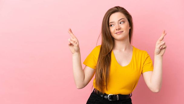 Adolescente menina sobre isolado fundo rosa com dedos cruzando e desejando o melhor - Foto, Imagem