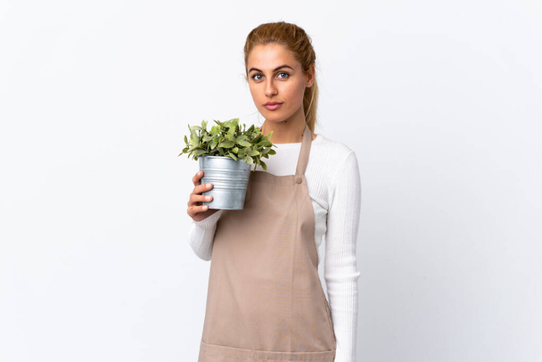 Sarışın, bahçıvan bir kadın, izole edilmiş beyaz arka plan üzerinde bir bitki tutuyor. Kollarını kavuşturuyor. - Fotoğraf, Görsel