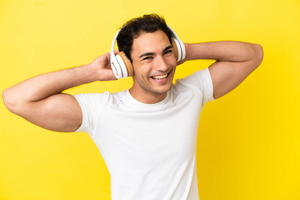 Caucásico guapo hombre sobre aislado amarillo fondo escuchar música - Foto, Imagen