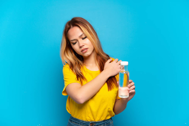 Ragazza adolescente con una bottiglia d'acqua su sfondo blu isolato che soffre di dolore alla spalla per aver fatto uno sforzo - Foto, immagini
