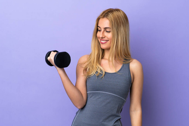 jong blond sport vrouw het maken van gewichtheffen over geïsoleerde paarse achtergrond met gelukkige uitdrukking - Foto, afbeelding