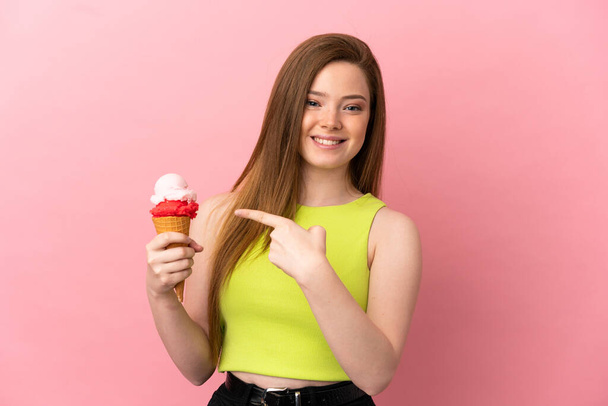 Ragazza adolescente con un gelato alla cornetta su sfondo rosa isolato che punta verso il lato per presentare un prodotto - Foto, immagini