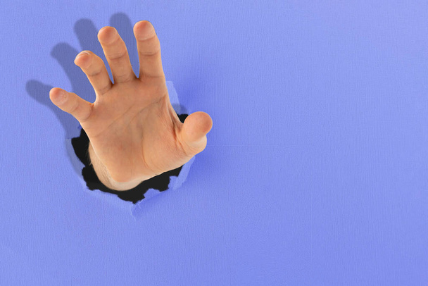 una mano humana llegar a la meta, elevar a través del agujero en el papel de color - Foto, Imagen