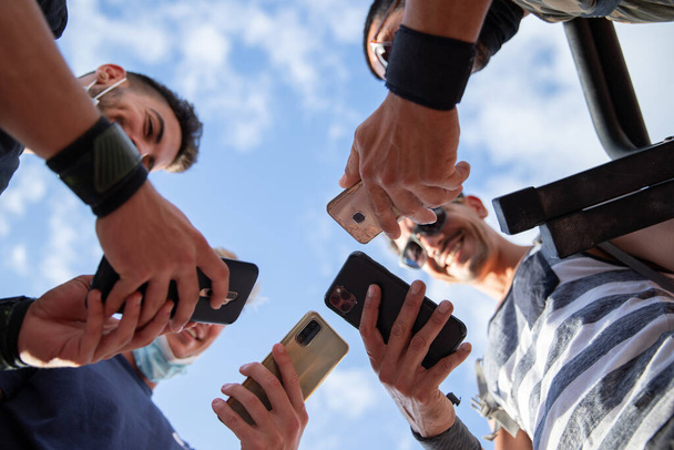 Een groep jonge sportieve mannen komen samen en gebruiken de smartphone, foto van onderen, groepsconcept, community en eenheid. - Foto, afbeelding