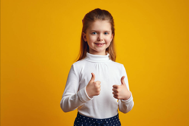 Cute kid with opened mouth showing thumbs up isolated on yellow wall - Photo, Image