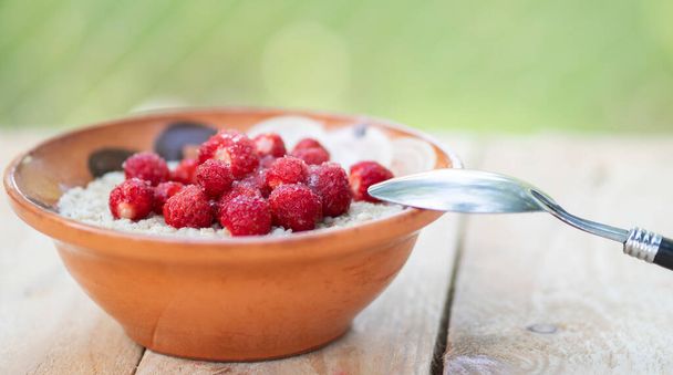 Bowl with oatmeal with strawberries on a wooden table in the garden. Selective focus. - 写真・画像