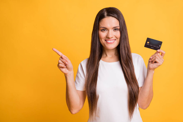 Photo portrait of beautiful latin woman showing debit card pointing finger empty space isolated on vibrant yellow color background - Foto, imagen