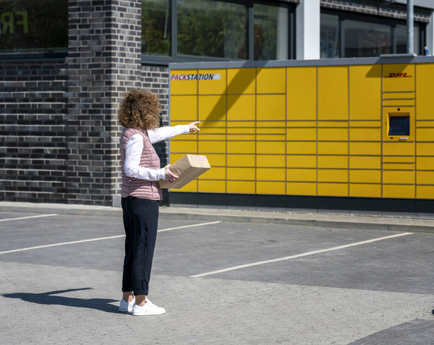a woman sends and receives a mail item at the typical yellow german packing stations of DHL - Photo, Image