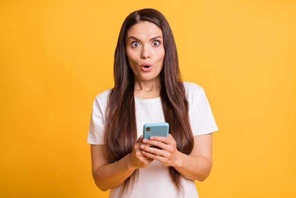 Photo portrait of amazed woman reading information in internet with cellphone staring isolated on bright yellow color background - Fotografie, Obrázek