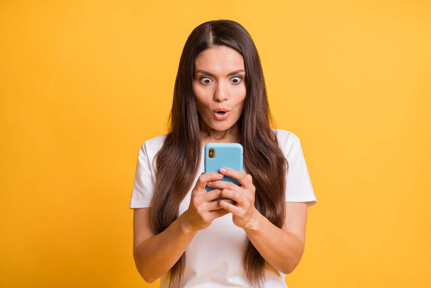 Photo portrait of shocked staring female influencer keeping smartphone reading fake news isolated on vivid yellow color background - Photo, Image