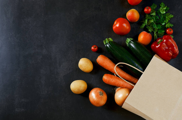 ショッピングや配信健康的な食品の概念。食品スーパーマーケットやきれいなビーガン食のコンセプト。新鮮な野菜や果物:ニンジン,ジャガイモ,ズッキーニ,黒の背景に紙袋にトマト.スペースのコピー. - 写真・画像