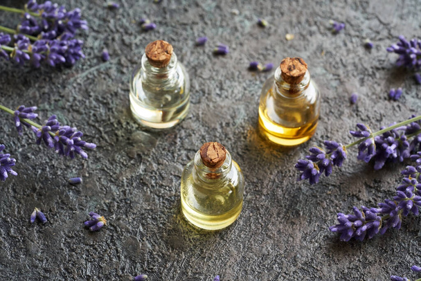Drie flessen etherische olie met verse bloeiende lavendel op een donkere achtergrond. Aromatherapie of kruidengeneeskunde. - Foto, afbeelding