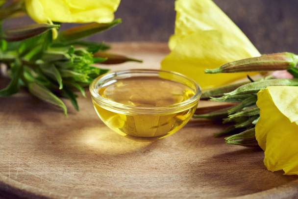 Evening primrose oil in a bowl, with blooming Oenothera biennis plant, with copy space - Photo, Image