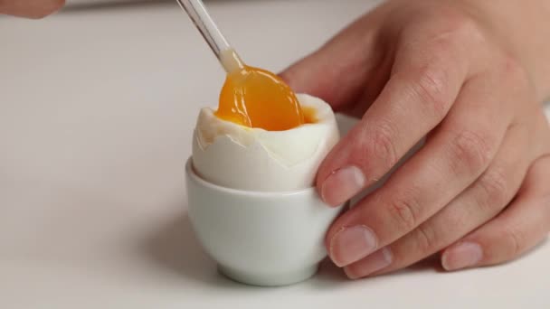 Mangia un uovo sodo da un guscio d'uovo rotto con un cucchiaio di vetro. Uovo di canna in tazza d'uovo - Filmati, video
