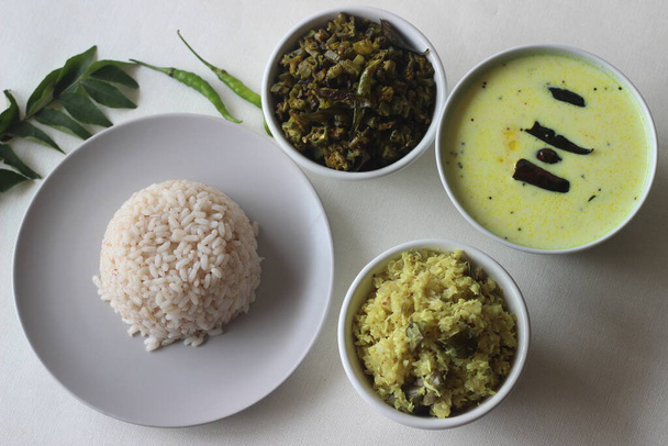 Vegetarian meals prepared in Kerala style. The serving includes boiled red rice, stir fried onions with grated coconut, stir fried okra, tempered buttermilk and poppadum. Shot on white background. - Photo, Image