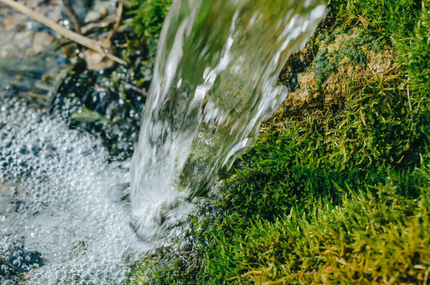 Wasserstrahl aus der Quelle vor dem Hintergrund von grünem Moosgras sauberes Wasser Ökologie Umweltprobleme Trinkwasser - Foto, Bild