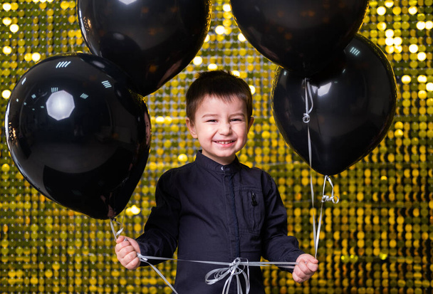 bambino ragazzo in possesso di palloncini neri su sfondo con paillettes oro lucido, paillettes - Foto, immagini