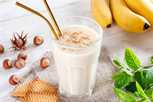 Delicious banana smoothie with sliced bananas and cookies in glass on a white background. Healthy breakfast. - Photo, Image