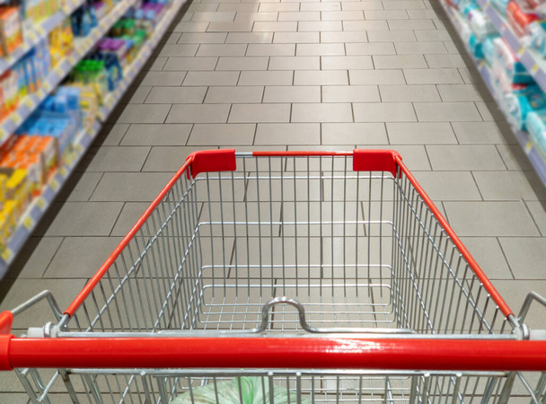 Supermarket aisle with empty red shopping cart. - Photo, Image