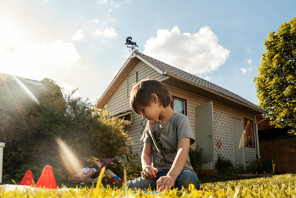 Il bambino in età prescolare gioca sull'erba verde con la casa sullo sfondo. - Foto, immagini