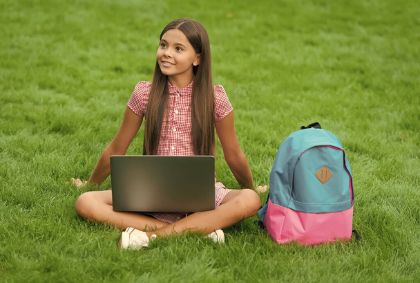 Young and carefree. Start up. child playing computer game. back to school. education online. knowledge day. kid learning private lesson. blogging. happy girl sitting on green grass with laptop - 写真・画像