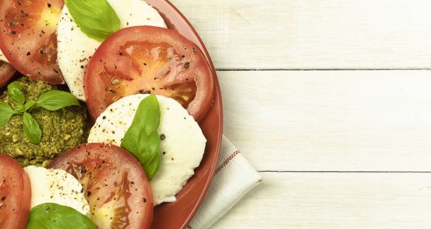 Caprese salaatti lautasella puinen tausta. Tuoretta tomaattia ja mozzarellajuustoa basilikanlehdillä lautasella. Salaatti puupöydällä. Top näkymä kopioi tilaa - Valokuva, kuva