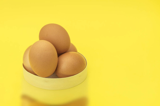 Rohe Hühnereier in einem Korb auf gelbem Hintergrund. Eier in einem Holzkorb auf gelbem Hintergrund. Frische Eier von einem Biohof. Hintergrund mit Platz für Text - Foto, Bild