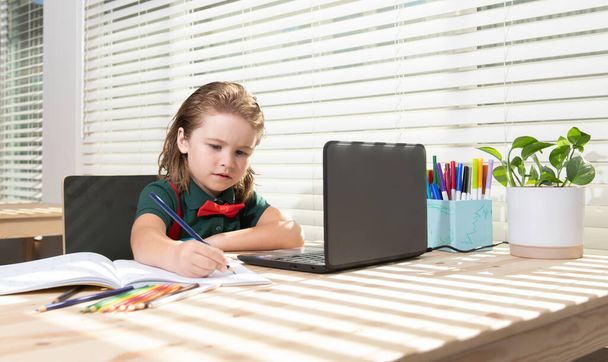 Cute schoolboy child does her homework with a tablet or laptop at home. Pupil writes the task in a notebook. Education and learning, kids home schooling. - Fotografie, Obrázek