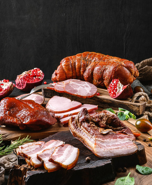 Assortment of cold meats products, ham, sausage, salami, parma, prosciutto, bacon on wooden cutting board with herb and spices over dark background. Meat appetizer, set of wine, close up - Photo, Image