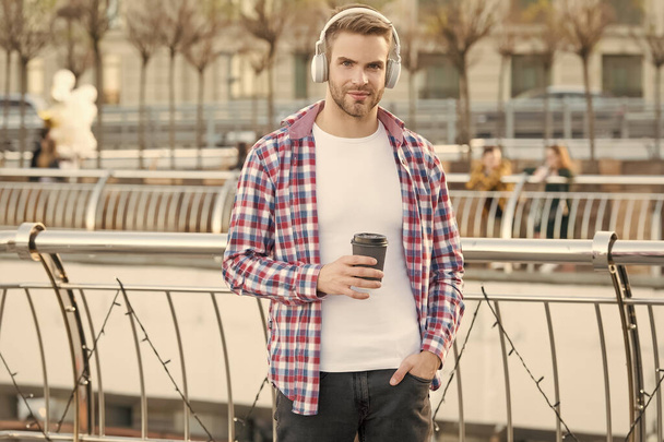 handsome young man wear headphones. casual dressed male drinking morning coffee from cup. unshaven guy with bristle listen music. urban style. modern life concept. student drink tea - Фото, зображення