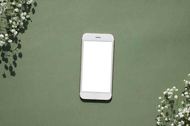 Mobile phone mock up on a pastel green background decorated with white small flowers top view - 写真・画像