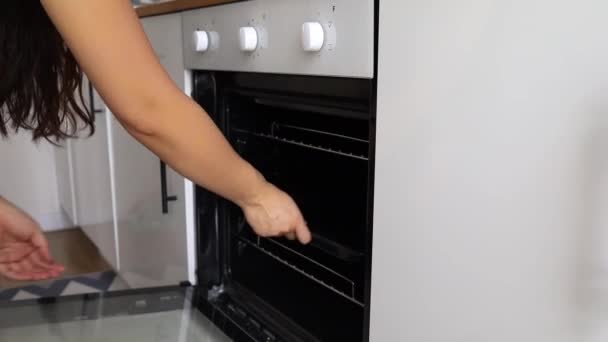 Mujer pone la cacerola con ingredientes crudos al horno calentado - Imágenes, Vídeo