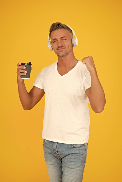 Live life to the full. Happy man hold coffee flexing arm. Strong coffee. Dark roast. Natural energy drink. Takeaway and cafe. Caffeine addicted. Listening to music. Modern technology. Cup of energy - Foto, Imagen