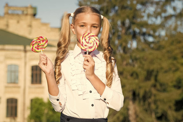 Happy student girl eat colorful lollipop outdoors, yummy dessert concept - Foto, Imagen