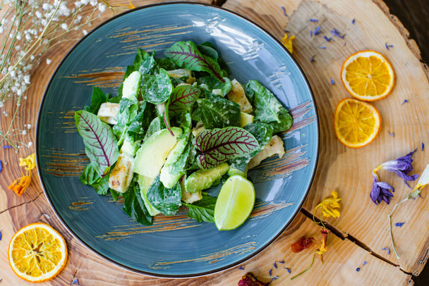 Summer menu. Salad with squid, spinach leaves, avocado slices and lime slice in a blue ceramic plate on a natural wooden background with citrus slices and dried flowers. - Photo, Image