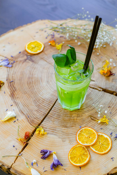 Des boissons d'été. Cocktail d'agrumes rafraîchissant vert avec céleri et concombre, glaçons et melissa dans un verre sur un fond de bois naturel avec un fond flou et un endroit pour le texte. - Photo, image