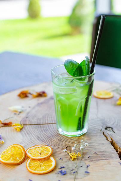 Summer drinks. Green refreshing citrus cocktail with celery and cucumber, ice cubes and melissa in a glass on a natural wood background with a blurred background and a place for text. - Foto, afbeelding