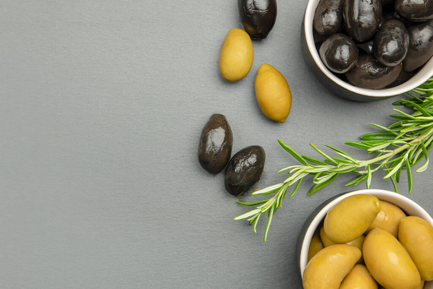 Black and green olives. Bella di cerignola Italian olives. Colored olives and a sprig of rosemary lie on a black stone countertop. Culinary banner or poster for advertising with place for text - Photo, image