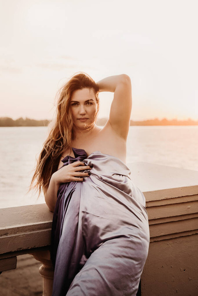 Beautiful young sexy woman wrapped in a blue blanket on the dawn near the water. woman with long healthy hair. Travel and Vacation. Freedom Concept - Фото, зображення