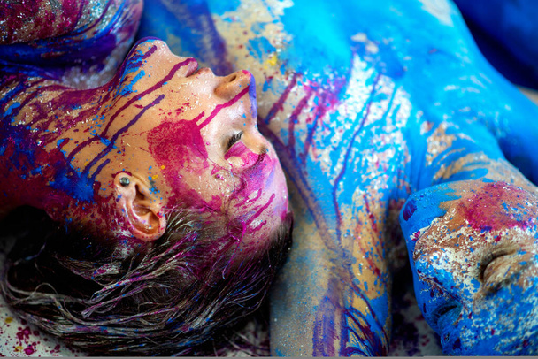 two strong colored portraits with blue purple magenta bodypainting, sexy brunette women, painted decorative, lying on the floor in the studio. Creative expressive abstract body painting art - Foto, Imagem