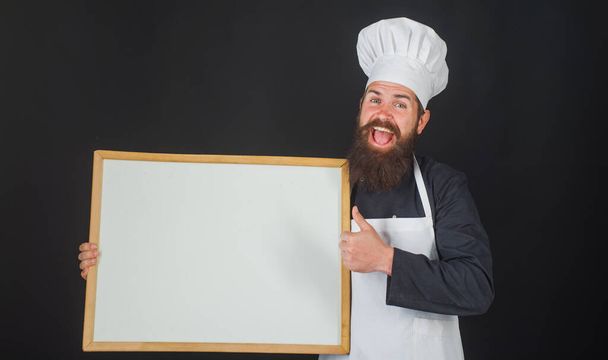 Szef kuchni z pustą tablicą menu. Uśmiechnięty kucharz lub piekarz pokazuje kciuk do góry. Reklama. Kopiuj miejsce na tekst. - Zdjęcie, obraz