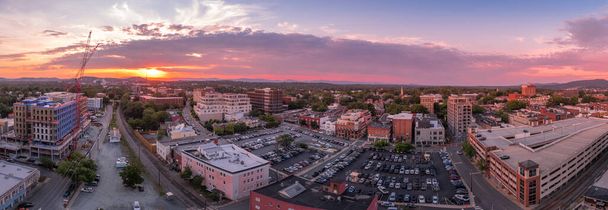 Vista aérea al atardecer del centro de Charlottesville, Virginia con edificio de apartamentos de oficinas de nueva construcción, estacionamiento en el mercado de la ciudad, estacionamiento y el centro comercial con el colorido cielo naranja púrpura dramático - Foto, imagen